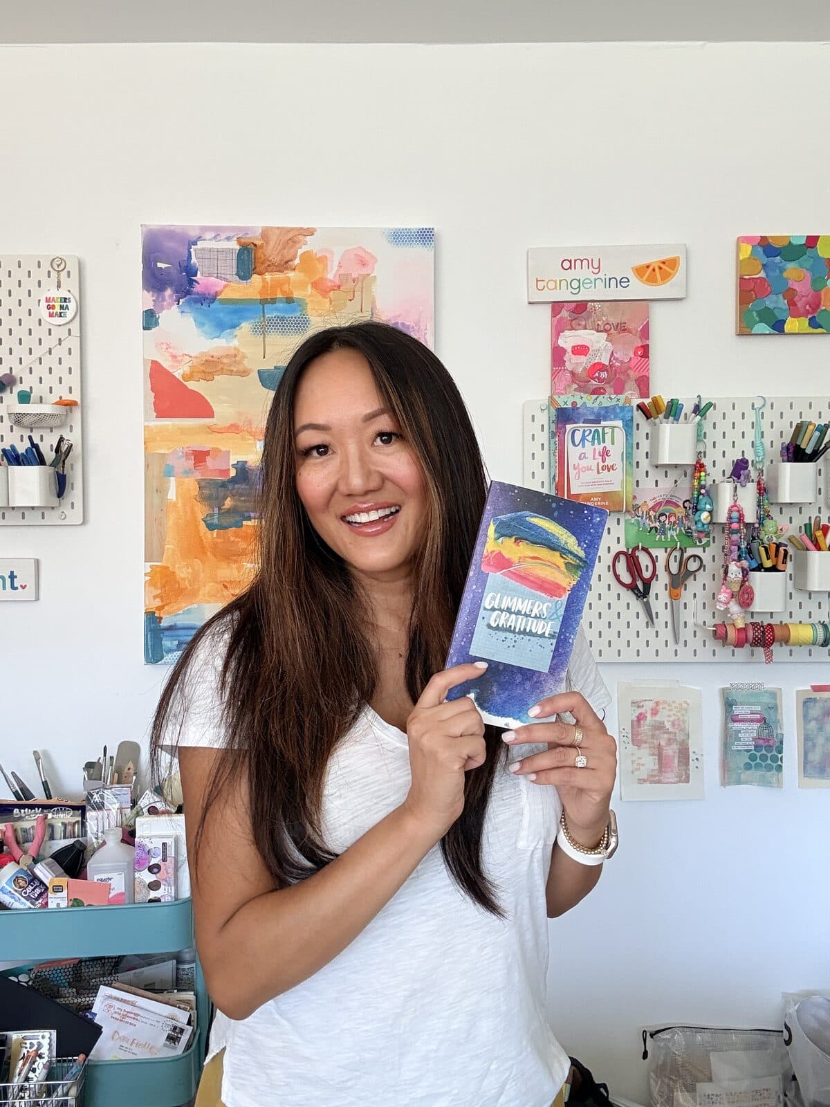 Amy Tangerine in her studio, holding her Glimmers and Gratitude journal